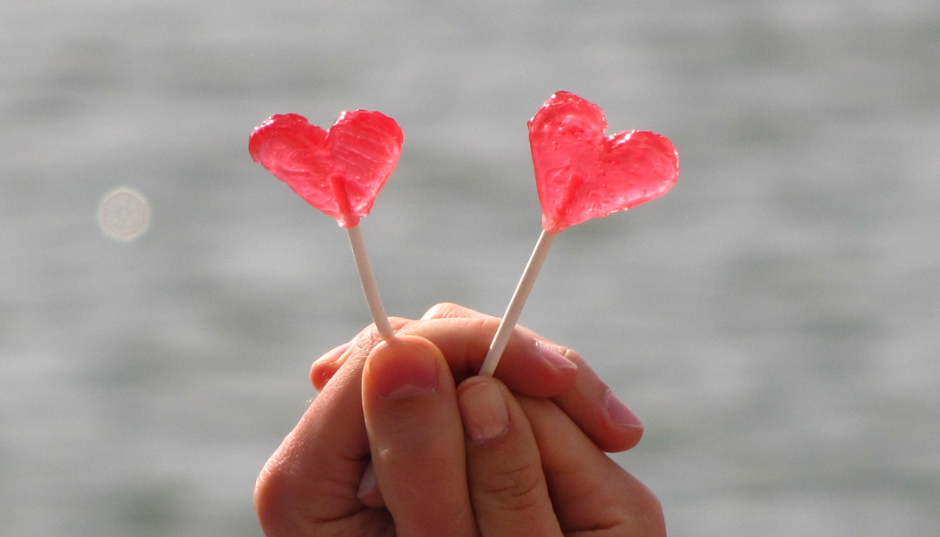 deux personnes qui tiennent chacun une sucette en forme de coeur