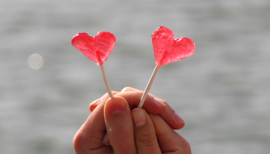 deux personnes qui tiennent chacun une sucette en forme de coeur